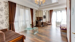 A spacious hotel room with a wooden floor, a glass coffee table, a sofa, a bed, a TV, and a balcony with curtains. - Bishkek Centrum Hotel (Bishkek)