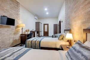 Una habitación de hotel con dos camas, un escritorio con silla, un televisor y un armario.
