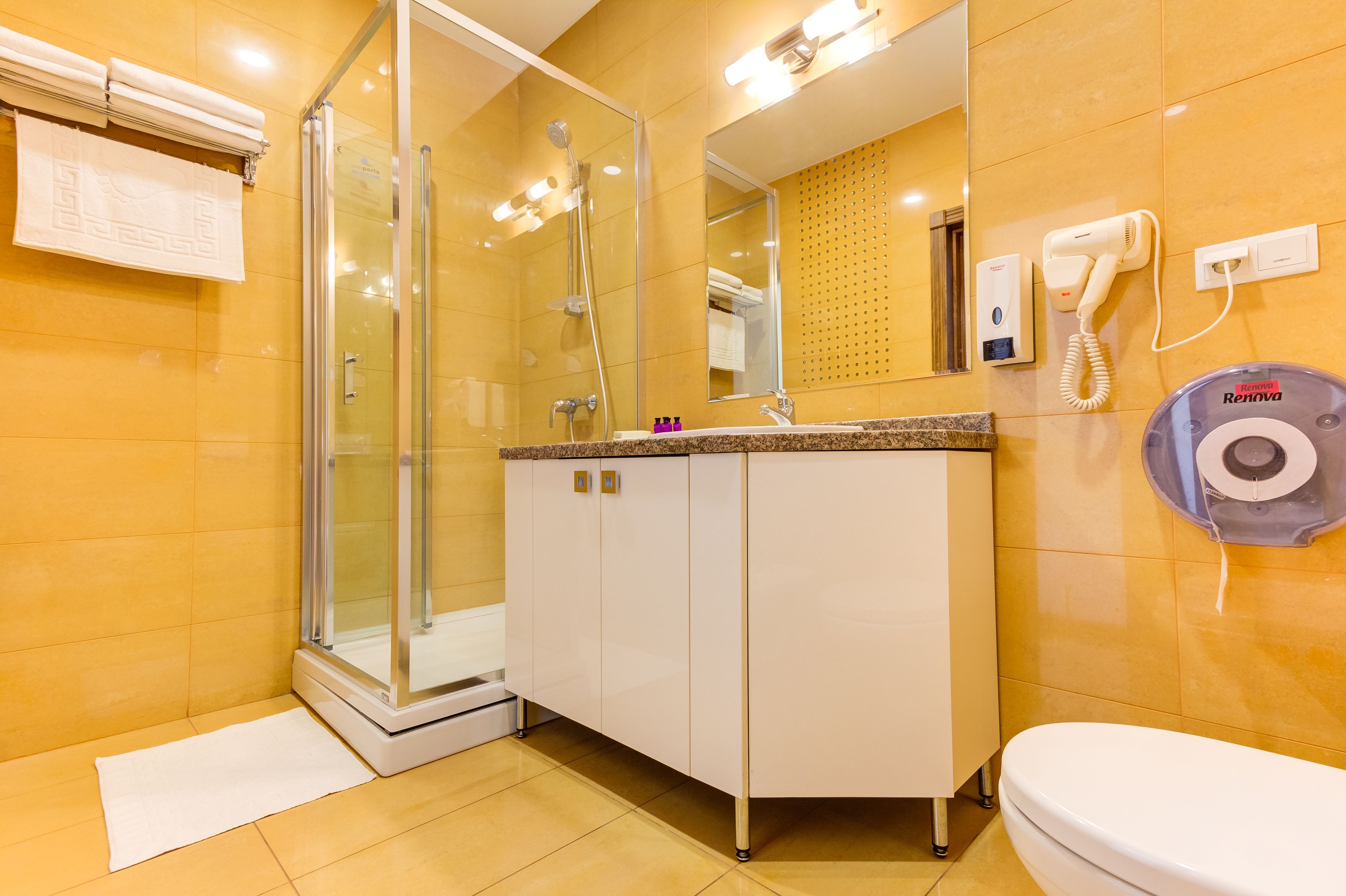 Ein modernes Badezimmer mit einer Duschkabine aus Glas, einem weißen Waschbecken mit Granitplatte, einer Toilette und einem an der Wand befestigten Föhn.