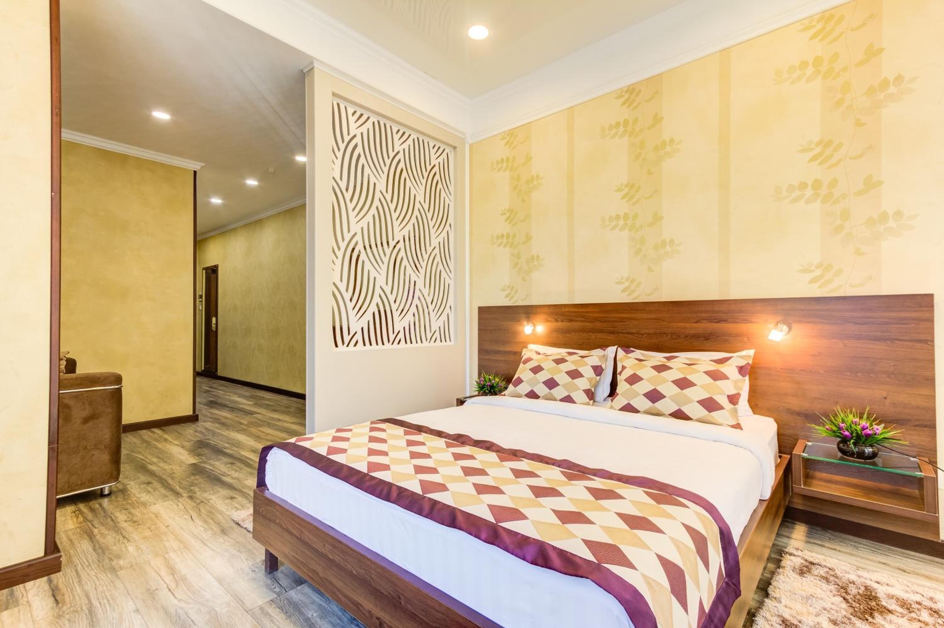 A hotel room with a wooden headboard, a patterned bedspread, and a decorative wall panel.