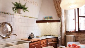 Une cuisine équipée d’un évier, d’une cuisinière et de meubles de rangement en bois. Il y a une fenêtre avec des rideaux et une plante suspendue au-dessus de l’évier.