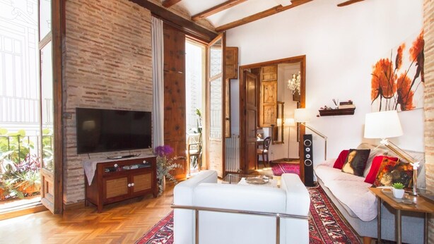 Un salon avec un téléviseur, un canapé blanc et un tapis rouge à motifs.