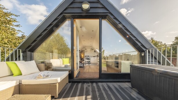 A modern, triangular-roofed outdoor living area with a sofa, a dining table, and a view into the interior. - Miller's Loft, A romantic retreat for 2 (Erpingham)