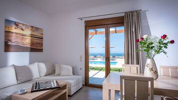 A modern living room with a sofa, a chess table, and a view of a pool and beach through a glass door.