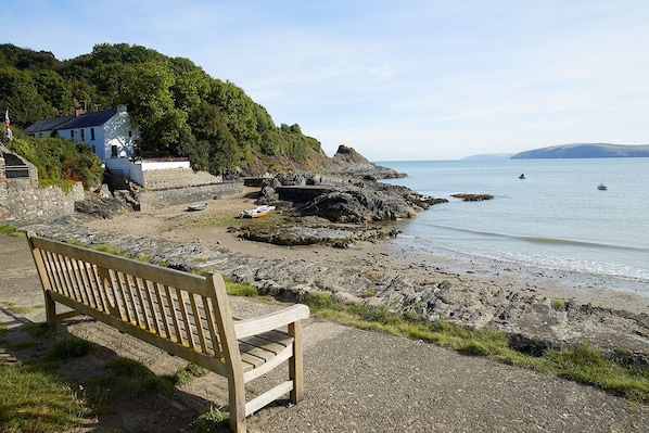 A bench on a rocky shore with a building and trees in the background.