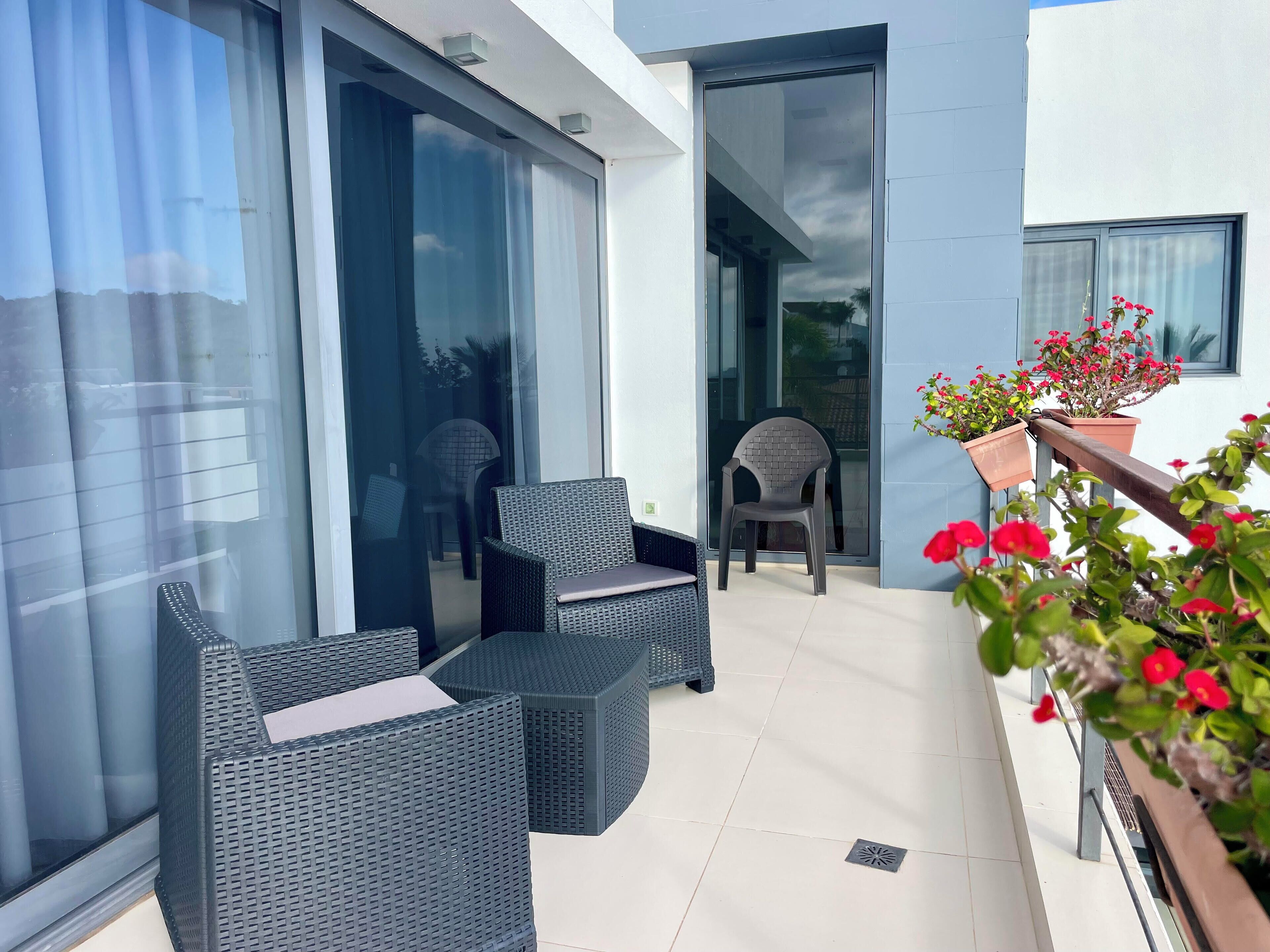 A balcony with wicker furniture, potted plants, and a glass door leading to an interior space.
