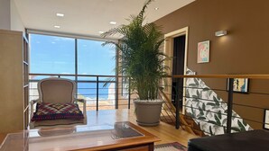 A room with a wooden desk, a chair, a large potted plant, a black sofa, a patterned rug, and a view of the ocean through large windows. - 5 Bedroom Villa With Heated Pool, Garden With BBQ & Views Over Hills And Ocean (Adeje)
