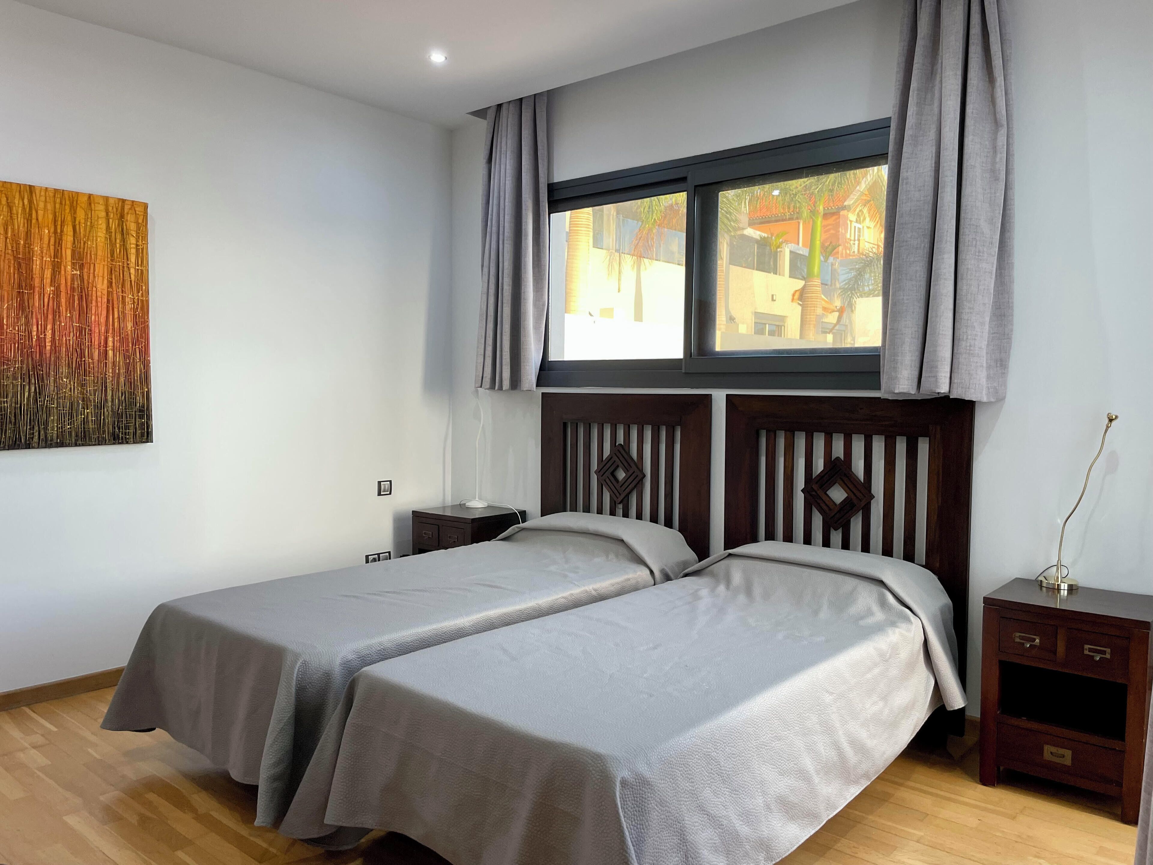 A hotel room with two beds, a window with curtains, a nightstand, and a wall-mounted artwork.