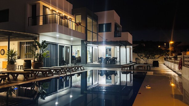 A modern building with a swimming pool, outdoor seating, and a well-lit entrance. - 5 Bedroom Villa With Heated Pool, Garden With BBQ & Views Over Hills And Ocean (Adeje)