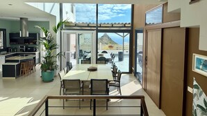 A modern kitchen with a large island, dining area with chairs, and a view of the ocean. - 5 Bedroom Villa With Heated Pool, Garden With BBQ & Views Over Hills And Ocean (Adeje)