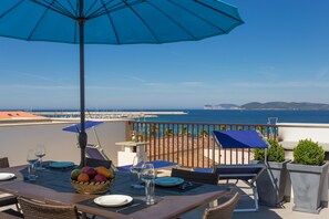 Un área de comedor al aire libre con una mesa preparada para dos personas, una sombrilla azul y vistas al mar.