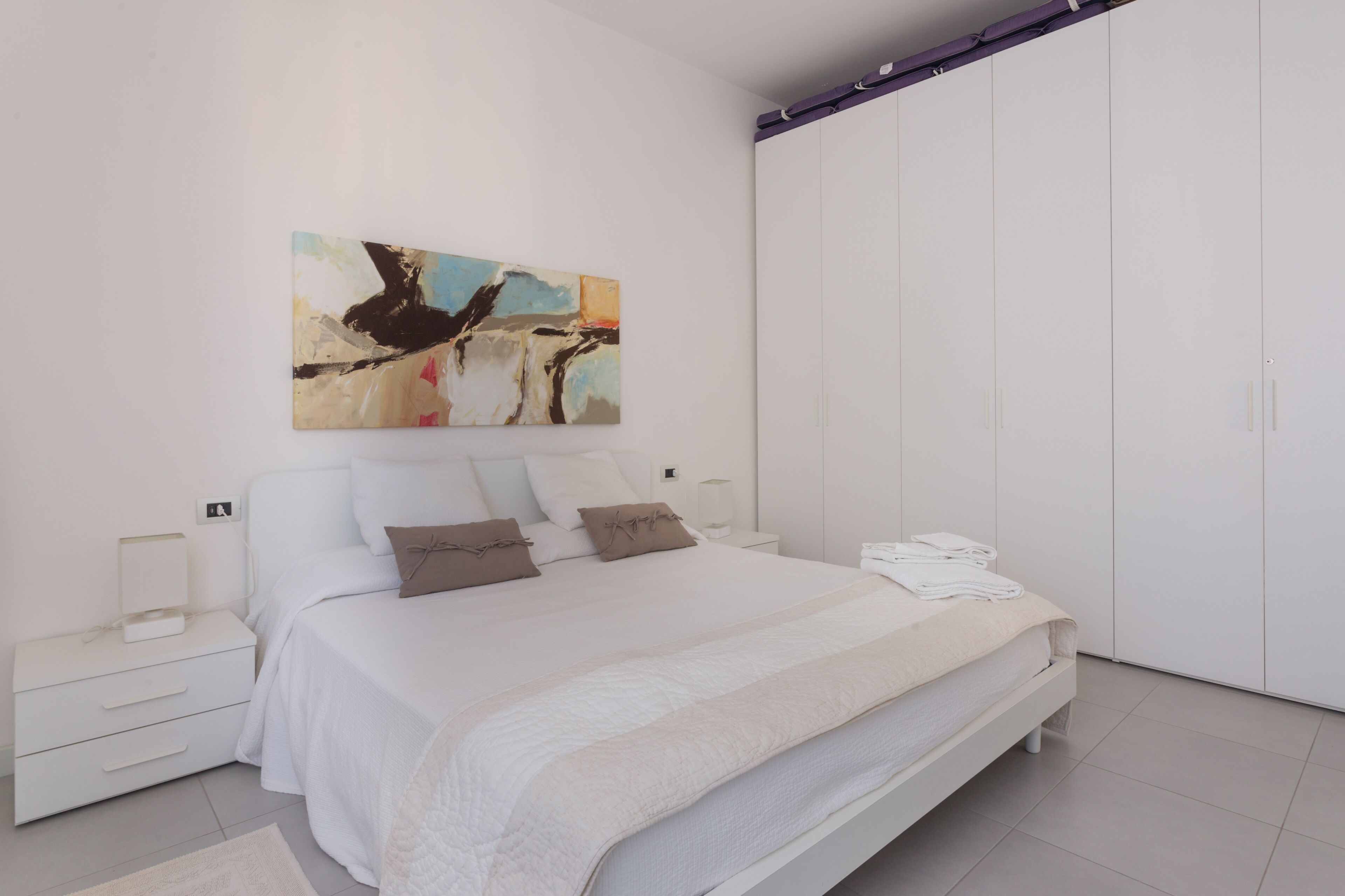 Ein modernes Schlafzimmer mit einem großen Bett, einem Nachttisch, einem Kleiderschrank und einem Bild an der Wand.