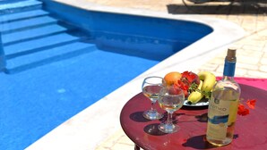 Et bord ved poolen med en hvid vinsflaske, to glas og et fad med frugt.