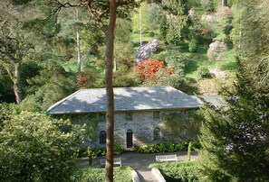 A stone building with a sloped roof, surrounded by dense greenery and trees.