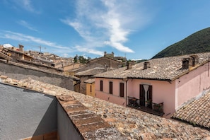 A traditional terracotta-tiled building with a pink facade, a balcony with potted plants, and a clear blue sky in the background. - TOP-ROOF LARGE APARTMENT IN SPOLETO CITY CENTER, QUIET AND COZY TO FEEL AT HOME (Spoleto)