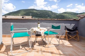 Une terrasse avec une table, des chaises et une bouteille de vin. La terrasse offre une vue sur un paysage montagneux.