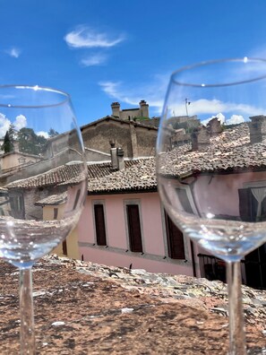 Two wine glasses on a table with a view of terracotta-roofed buildings and a clear blue sky. - TOP-ROOF LARGE APARTMENT IN SPOLETO CITY CENTER, QUIET AND COZY TO FEEL AT HOME (Spoleto)