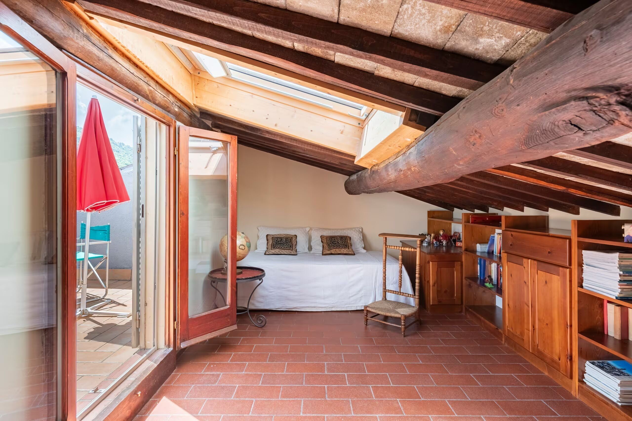 Un dormitorio acogedor en el ático con tragaluces, una cama, una mesita pequeña y una estantería.