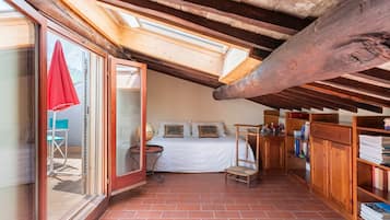 Une chambre mansardée chaleureuse, avec un puits de lumière, un lit, une petite table et une bibliothèque.