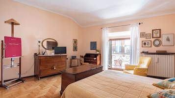 Une chambre avec un lit, un bureau, une chaise, une commode, une télévision et un balcon avec vue.