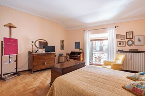 Une chambre avec un lit, un bureau, une chaise, une commode, une télévision et un balcon avec vue.