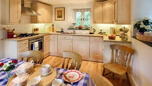 A kitchen with wooden cabinets, a dining table set with tea service, and a window with a view of greenery. - Tyddyn Derwen, Bodnant Estate, Colwyn Bay, Conwy, Wales (Colwyn Bay)