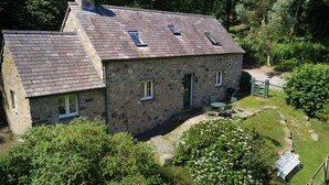 A stone house with a sloped roof, multiple windows, and a small garden area with a bench and pathway. - Tyddyn Derwen, Bodnant Estate, Colwyn Bay, Conwy, Wales (Colwyn Bay)