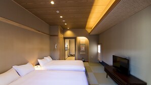 A hotel room with two beds, a TV on a wooden console, and a bathroom visible through an open door. - My K House (Kyoto)