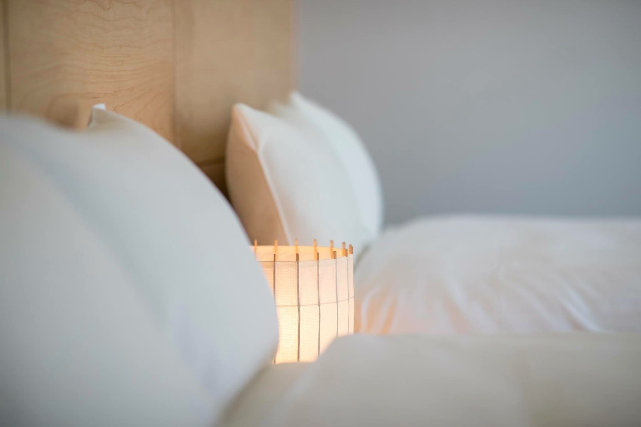 A bed with white bedding and a small, square, wooden-framed lamp.