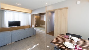 A modern hotel room with a sofa, a dining table set for two, and a television. - My K House (Kyoto)