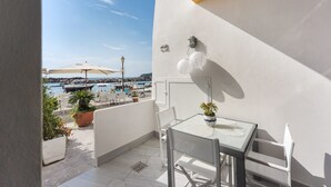 Een balkon met een tafel en stoelen, plantenbakken en uitzicht op zee en boten.
