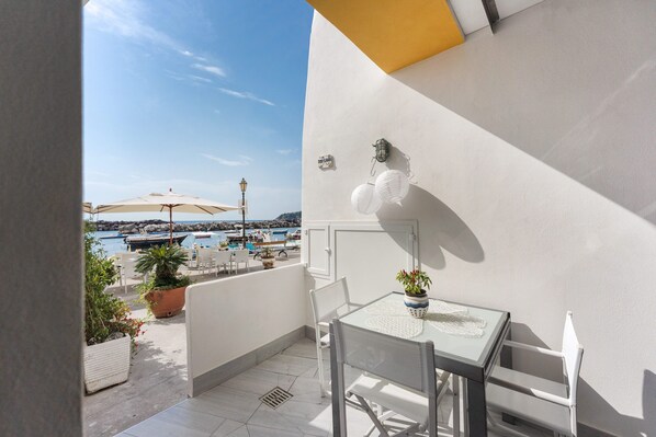A balcony with a table and chairs, potted plants, and a view of the sea and boats. - Loft Open Space in Corricella (Procida)