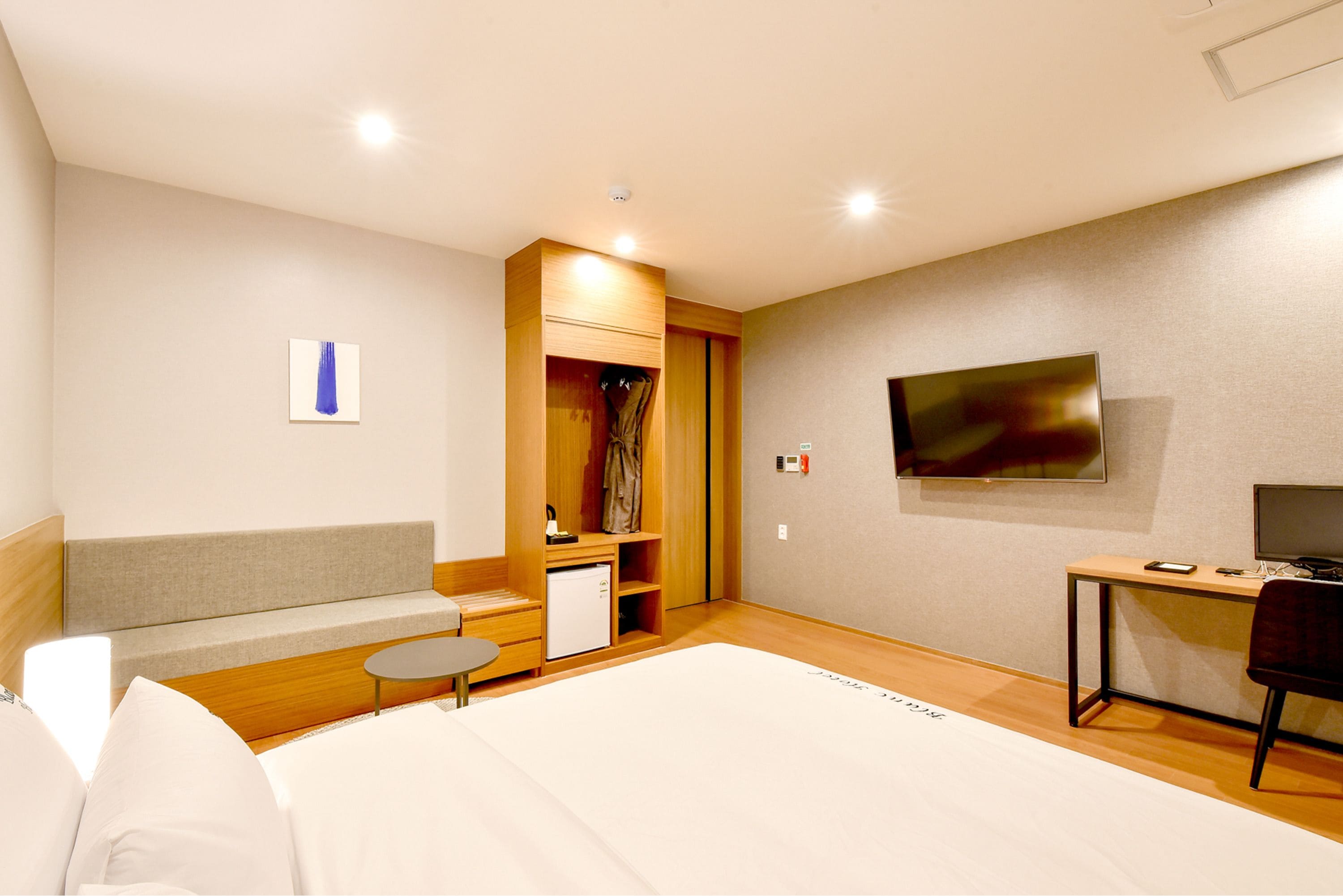 A modern hotel room with a bed, a desk, a TV, a small table, and a wardrobe.
