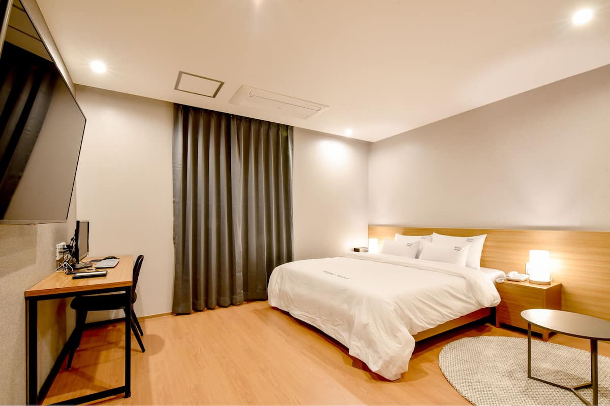 A hotel room with a bed, bedside table, desk, chair, and curtains.