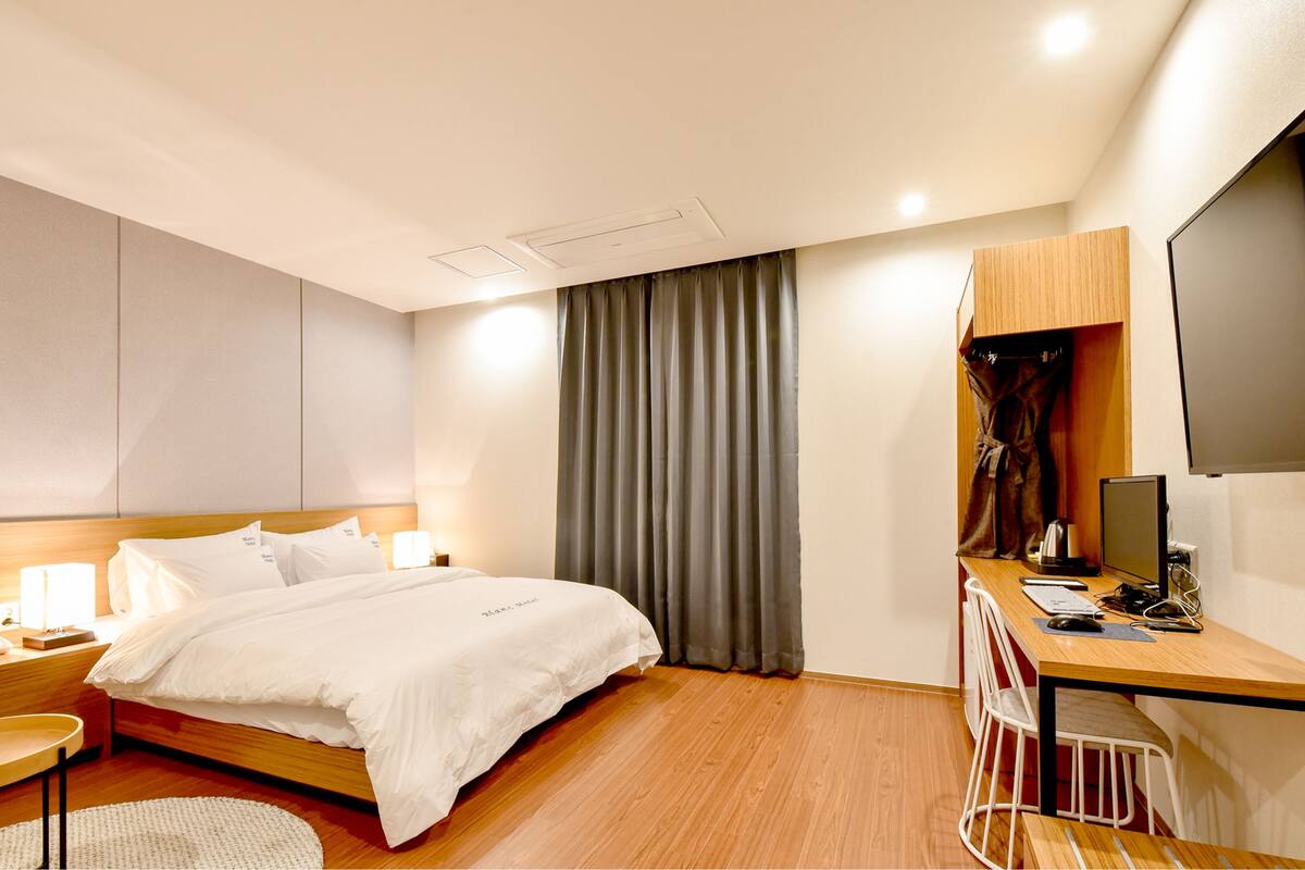 A modern hotel room with a wooden bed, a desk with a computer, and a TV.