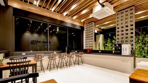 Un área de bar moderna con vigas de techo de madera, un gran ventanal con letrero 'NICE HOTEL', taburetes y una máquina de café.