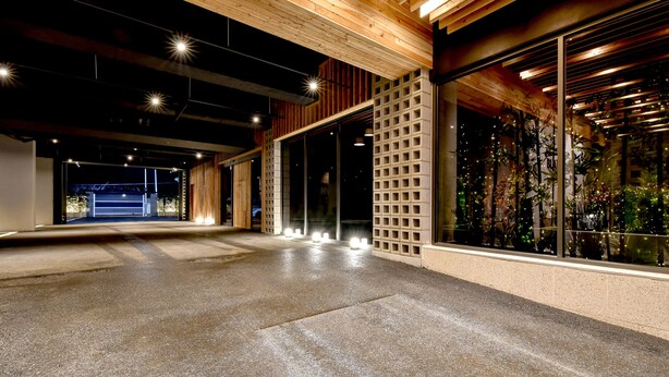 Amplio espacio interior con suelo de hormigón, vigas de madera en el techo y grandes ventanales con vistas a zonas verdes.