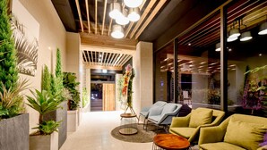 Un vestíbulo moderno con techo de madera, plantas en macetas, zona de estar y una pared de vidrio con luces interiores.