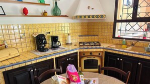 Una cocina con baldosas amarillas, estufa a gas, cafetera y lavamanos.