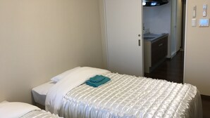 A hotel room with two beds, a kitchenette, and a bathroom visible through an open door. - Weekly Harbor View Mansion Ginowan (Ginowan)