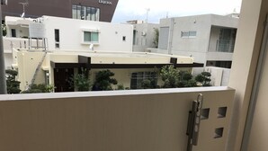 A balcony with a metal railing, a small trash bin, and a view of neighboring buildings. - Weekly Harbor View Mansion Ginowan (Ginowan)