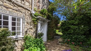 A stone building with a white door and window, surrounded by lush greenery and a garden with various plants and flowers. - Grove Cottage -  a cottage that sleeps 4 guests  in 2 bedrooms (Yarmouth)