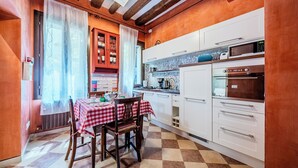 A kitchen with white cabinets, a microwave, and a stove. There is a dining table with a red and white checkered tablecloth and two chairs. - Campiello Tron Peaceful House (Venezia)