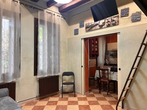 A room with a radiator, a chair, a table with chairs, a ladder, and a door leading to a kitchen area. - Campiello Tron Peaceful House (Venezia)