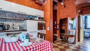 A kitchen with white cabinets, a microwave, and a coffee maker. There is a dining table with a red and white checkered tablecloth and various breakfast items. - Campiello Tron Peaceful House (Venezia)