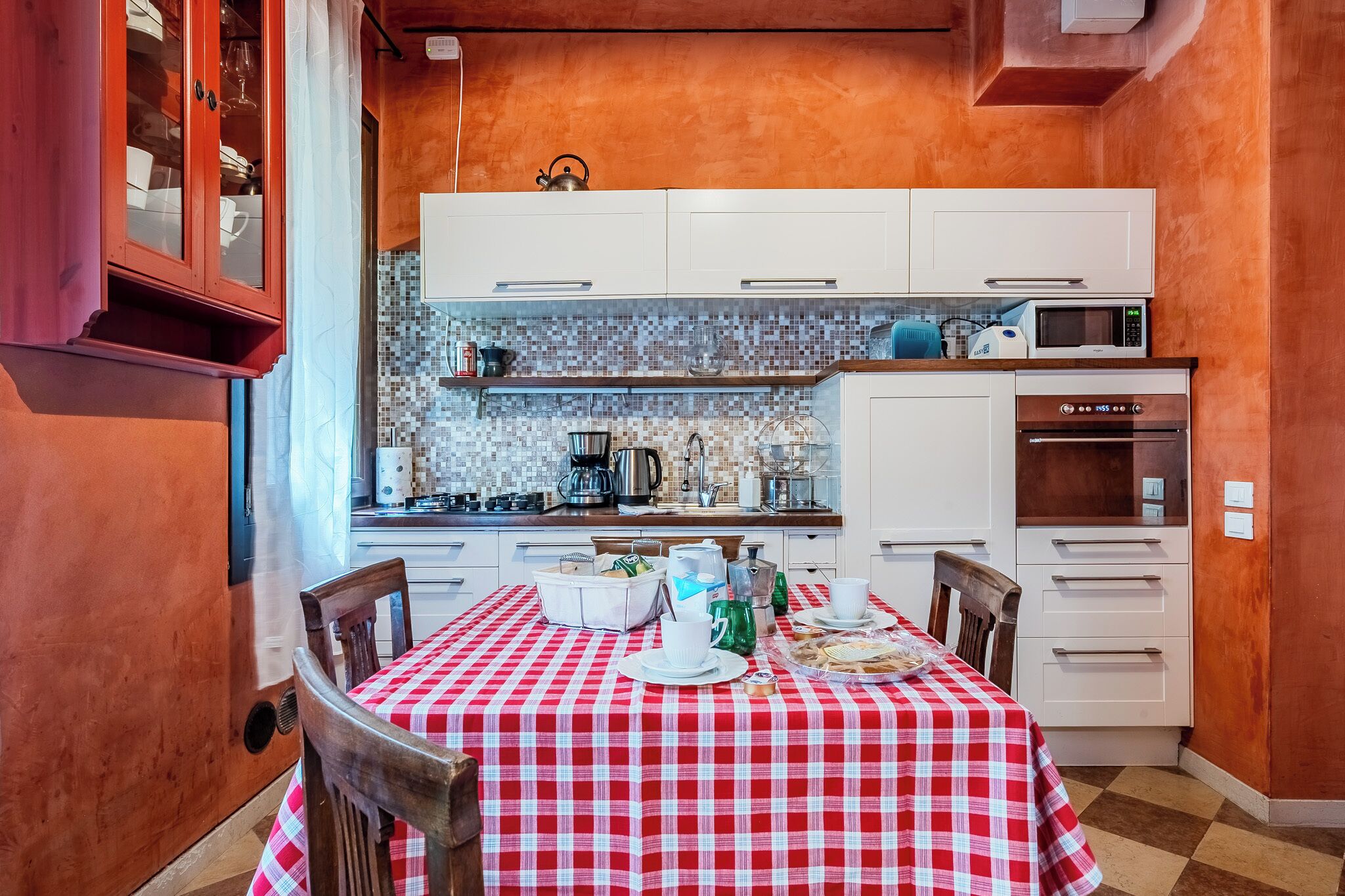 Cuina amb armaris blancs, un mantell daurat i blanc a quadres i un rebedor de rajoles.