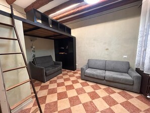 Ein Zimmer mit kariertem Boden, einem grauen Sofa, einem schwarzen Sofa, einer Leiter und einem Holzbalken an der Decke.