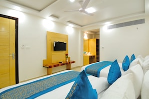 A hotel room with a bed, a TV mounted on the wall, a desk with a chair, and a bathroom visible through an open door. - The Gold Inn (New Delhi)
