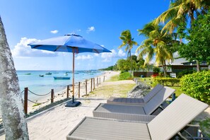 A beachside lounge area with lounge chairs, a blue umbrella, and a view of the ocean and boats.