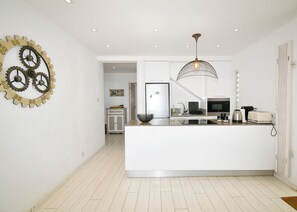 A modern kitchen with a central island, a hanging light fixture, and a wall-mounted clock.